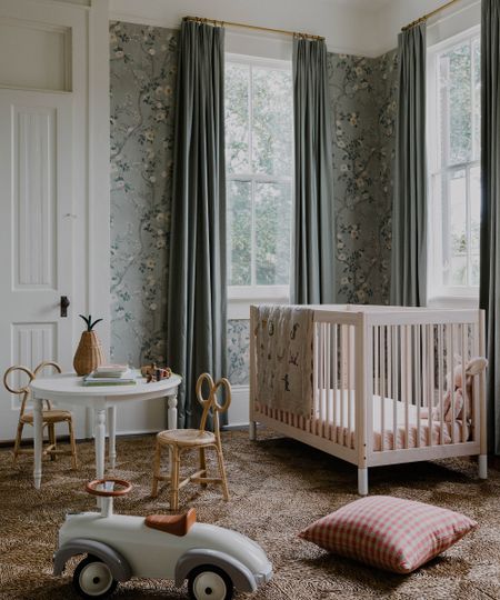 kid's bedroom with cot in one corner, toys on the floor and floral wallpaper on the walls