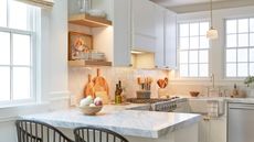 A small white peninsula kitchen with marble countertops and wooden decor