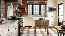 a country kitchen with painted checkerboard floors, white cabinetry, and a butcher block portable cart at the center
