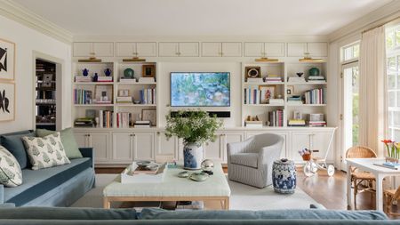 Living room with built-in tv unit with bookshelves, blue sectional sofa, coffee table and striped armchair