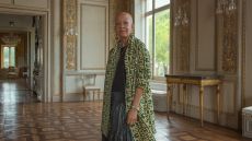 Shelia Bridges looking to camera wearing a green coat in a grand palazzo