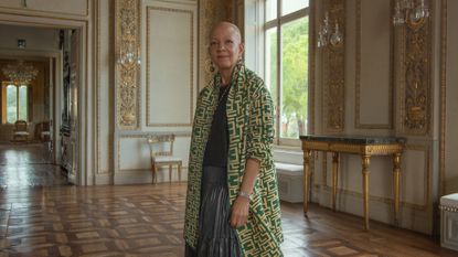 Shelia Bridges looking to camera wearing a green coat in a grand palazzo